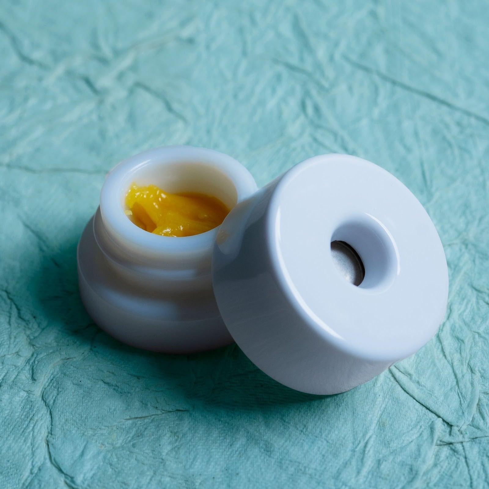 White Pop-Vac jar filled with a concentrate badder on a textured green surface